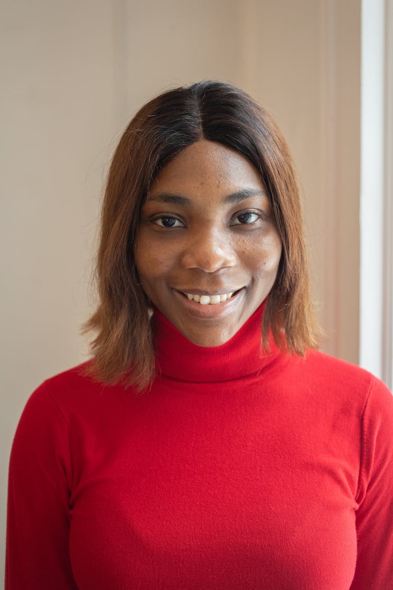 Smiling young woman in a red turtleneck gazing at the camera indoors, exuding confidence and joy.